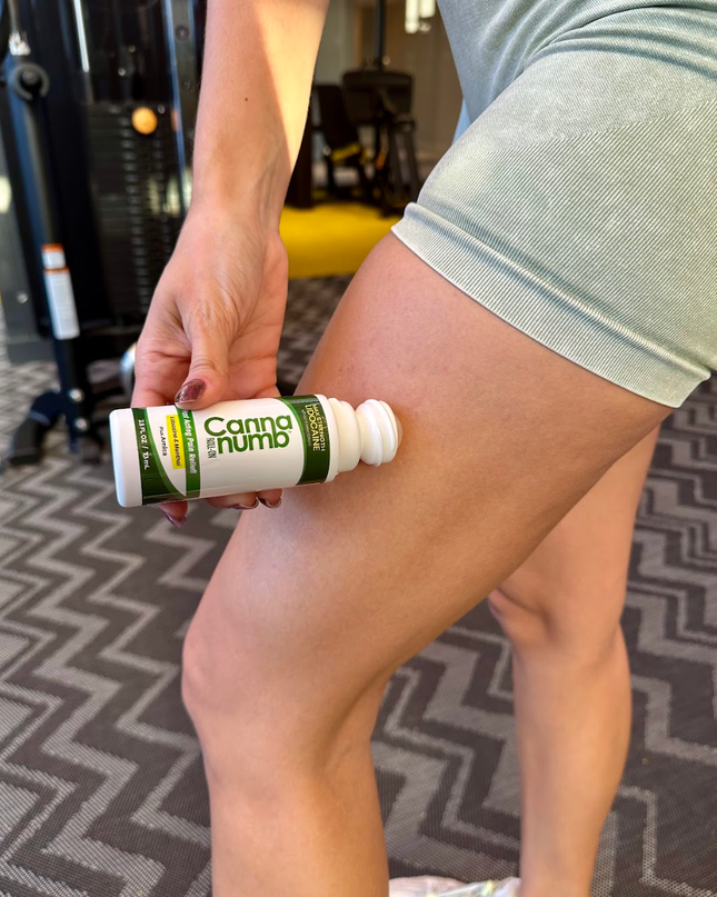 Person holding a bottle labeled 'Canna Numb' on a gym floor.
