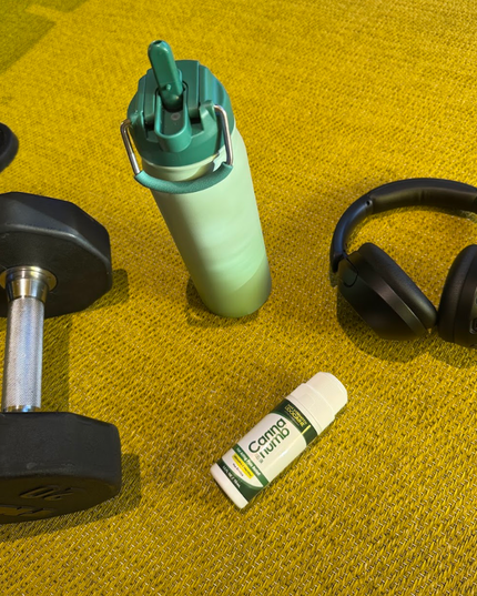 Green water bottle, black dumbbell, white and green tube, and black headphones on a yellow surface