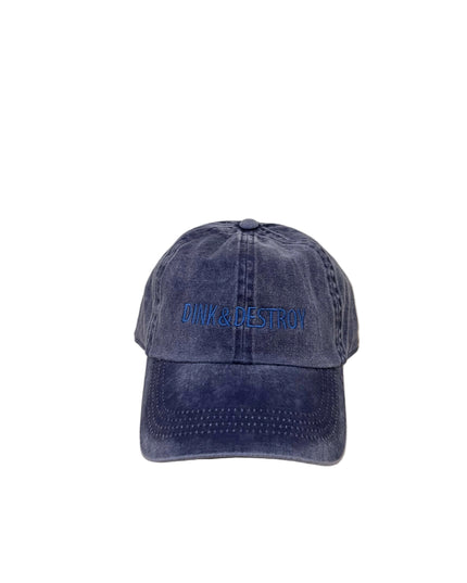 Blue denim cap with 'Pink & Destroy' embroidery on a wooden surface.