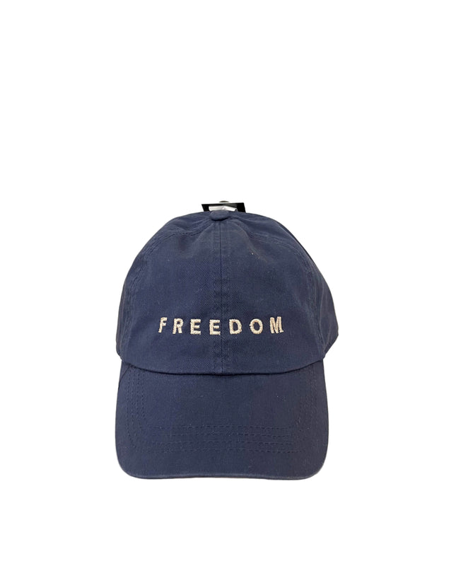 Navy blue cap with 'FREEDOM' text on a wooden surface and beige background