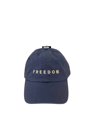 Navy blue cap with 'FREEDOM' text on a wooden surface and beige background