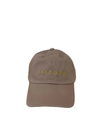 Brown cap with 'FREEDOM' embroidered on it, placed on a wooden surface with a beige wall background.
