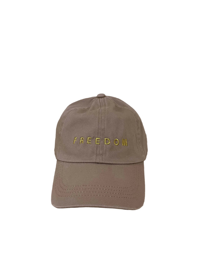 Brown cap with 'FREEDOM' embroidered on it, placed on a wooden surface with a beige wall background.