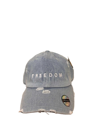 Blue denim cap with 'FREEDOM' text on a wooden surface